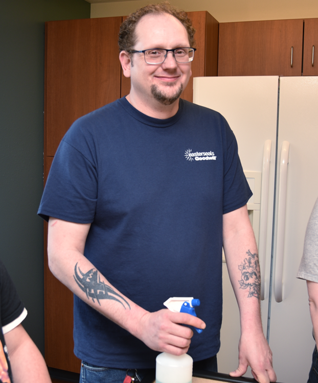 Chris smiling in a kitchen, holding cleaning supplies.