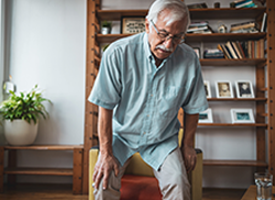 Elderly man bent over holding his knee in pain